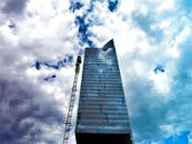 高层建筑的反光立面映衬着动态多云的天空，旁边还立着起重机