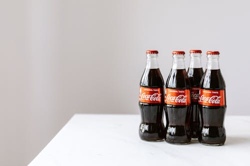 Curve shaped glass bottles of cold cola placed on white table against gray background