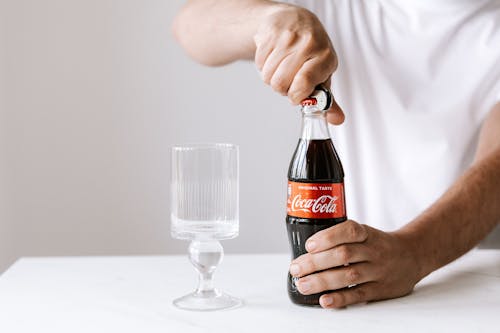 Crop man opening glass bottle of cola