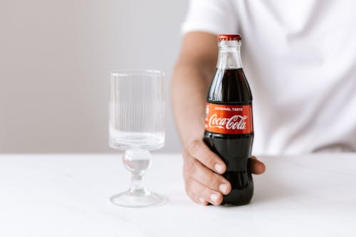 Free Crop unrecognizable young guy in white t shirt demonstrating bottle of cold coke Stock Photo