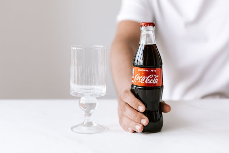 Crop Man Sitting At Table With Glass And Cola Bottle