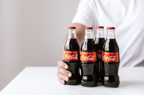 Free Crop anonymous young male in white t shirt demonstrating glass bottles of coke while sitting at table Stock Photo