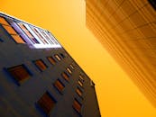 低角度视角下的现代城市建筑，玻璃倒影映衬着橙色天空