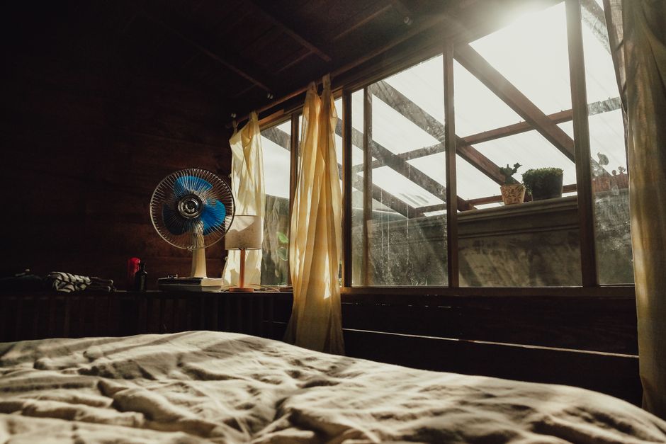 Schlafzimmer mit leichter Bettwaesche und Ventilator fuer besseren Schlaf bei Sommerhitze