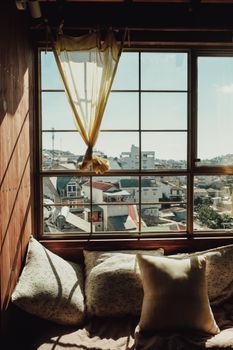 Comfortable window seat with pillows overlooking a city through a large window.