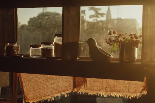 Free A warm-toned window scene featuring jars, a bird figurine, and flowers, catching sunlight. Stock Photo