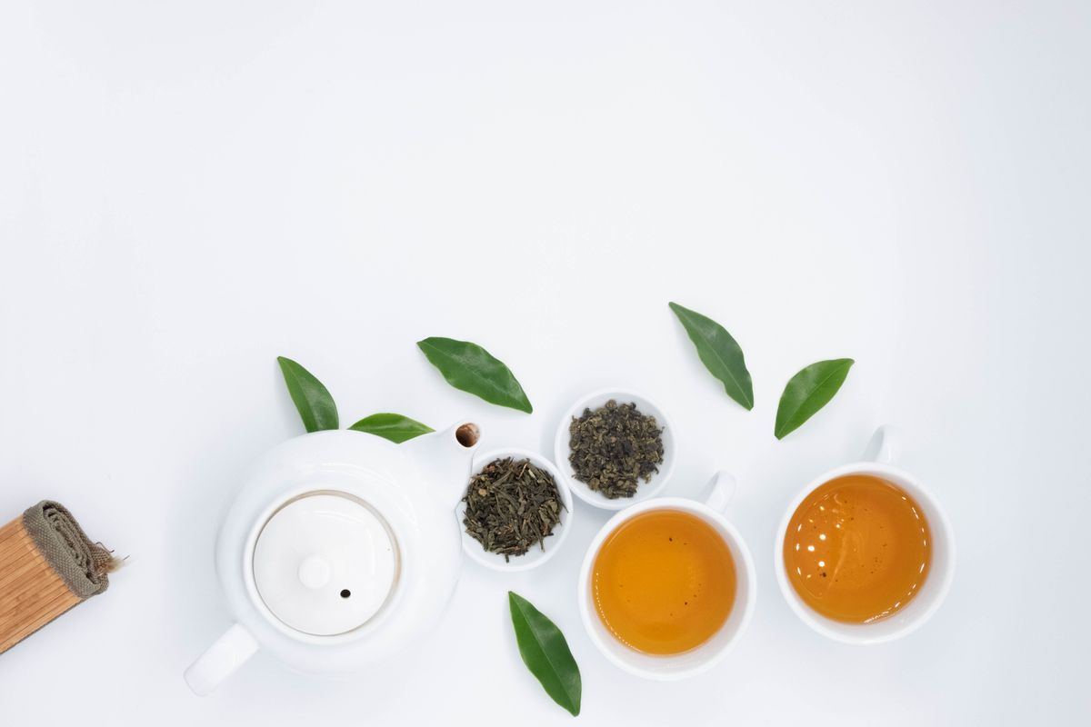 Green tea, loose tea leaves and tea accessories on a white table