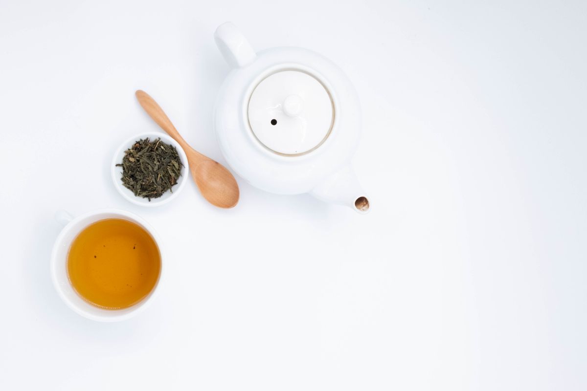 Green tea, teapot and loose tea leaves on a white surface