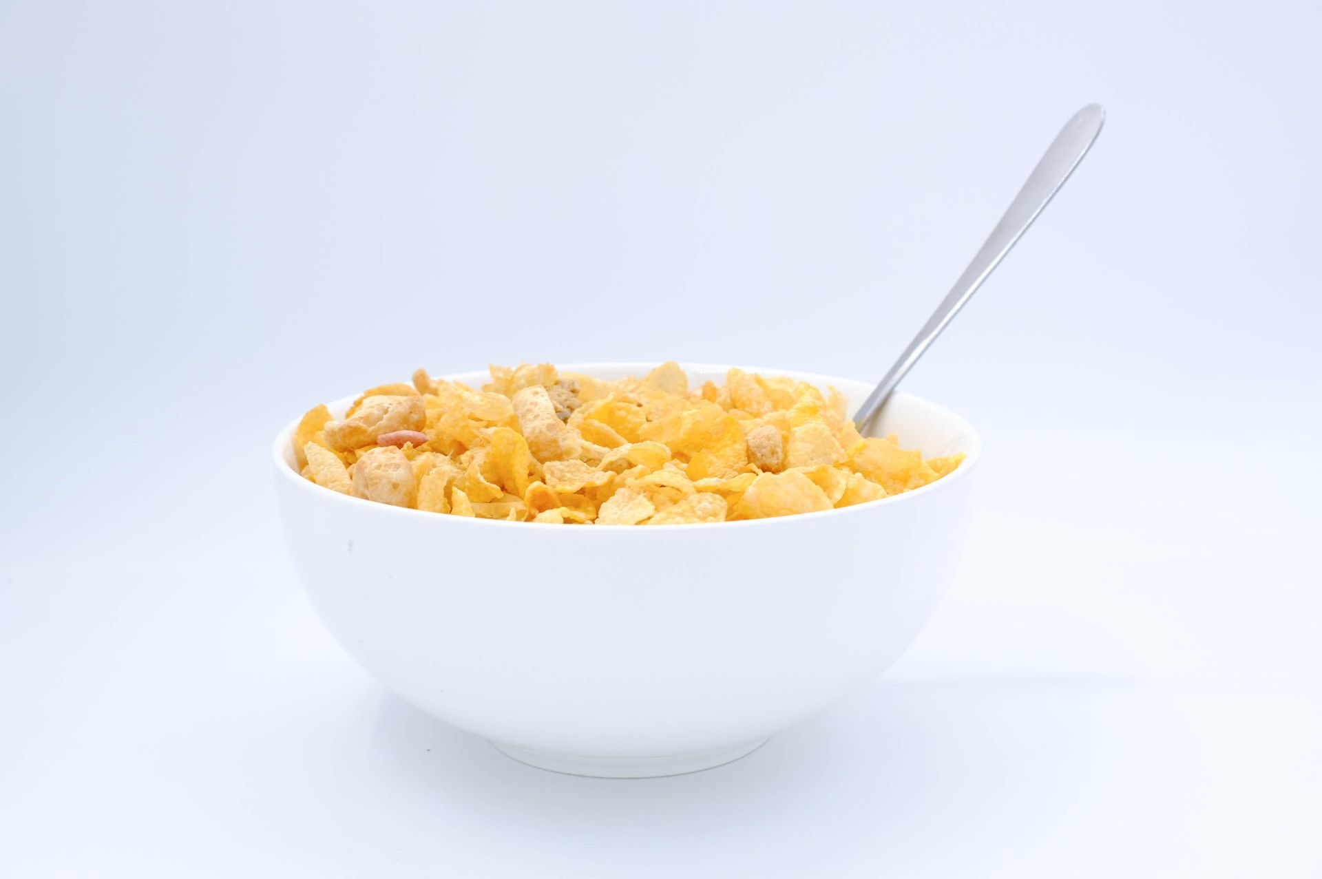 Bowl with cornflakes and spoon on white background