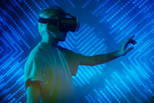 Man in White Crew Neck T-shirt Wearing Black VR Goggles on Blue Background