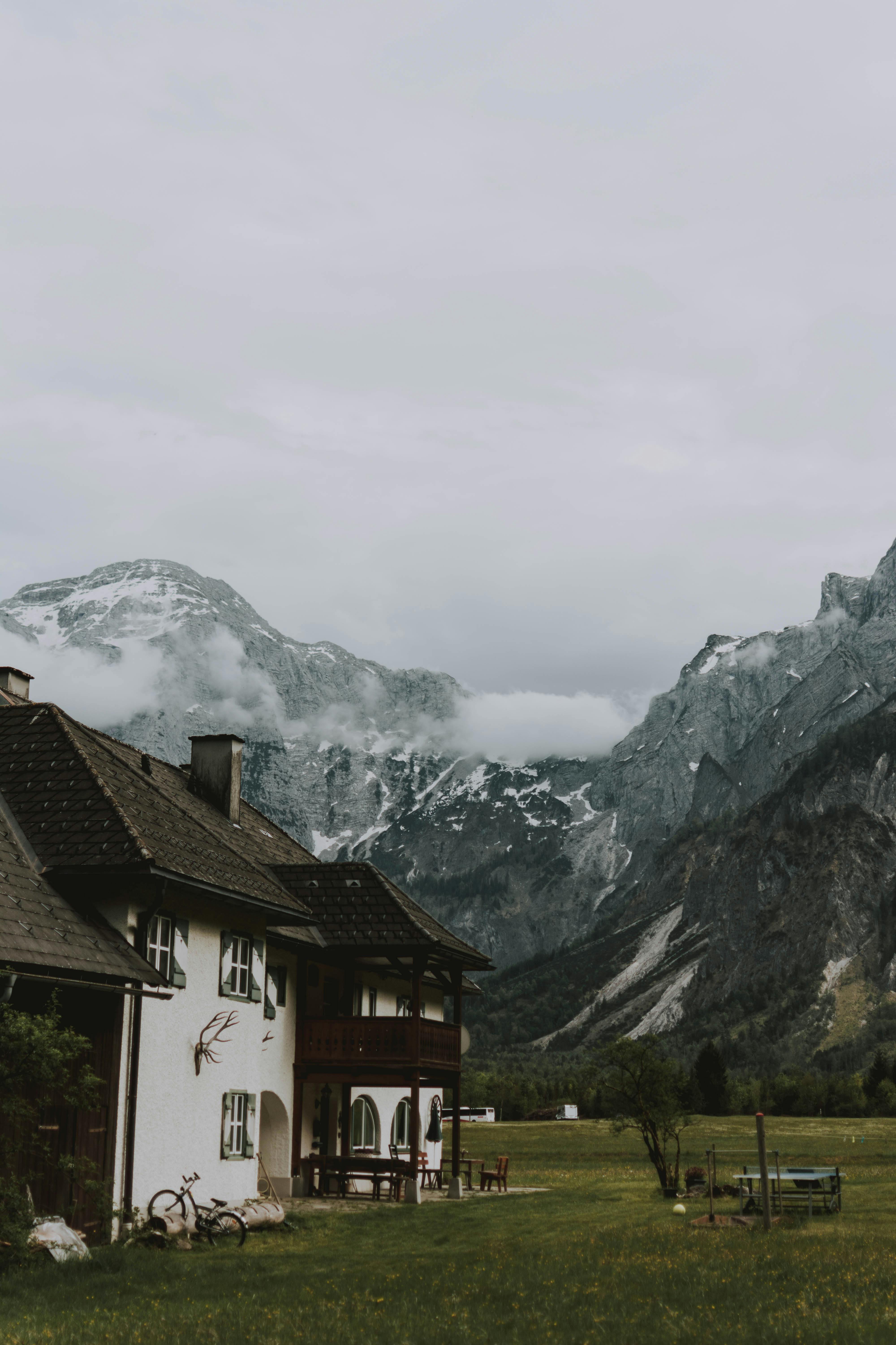 old house on meadow near snowy mountains under cloudy sky