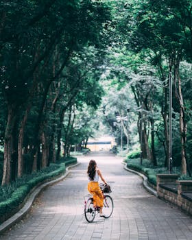 A woman rides a vintage bicycle along a tree-lined park path in summer.