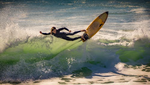 Full body of male surfer in wetsuit riding surfboard on foamy sea waves in summer day