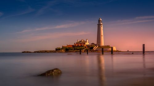 Free Picturesque view of lighthouse building located under evening sky with clouds near calm reflective sea water Stock Photo