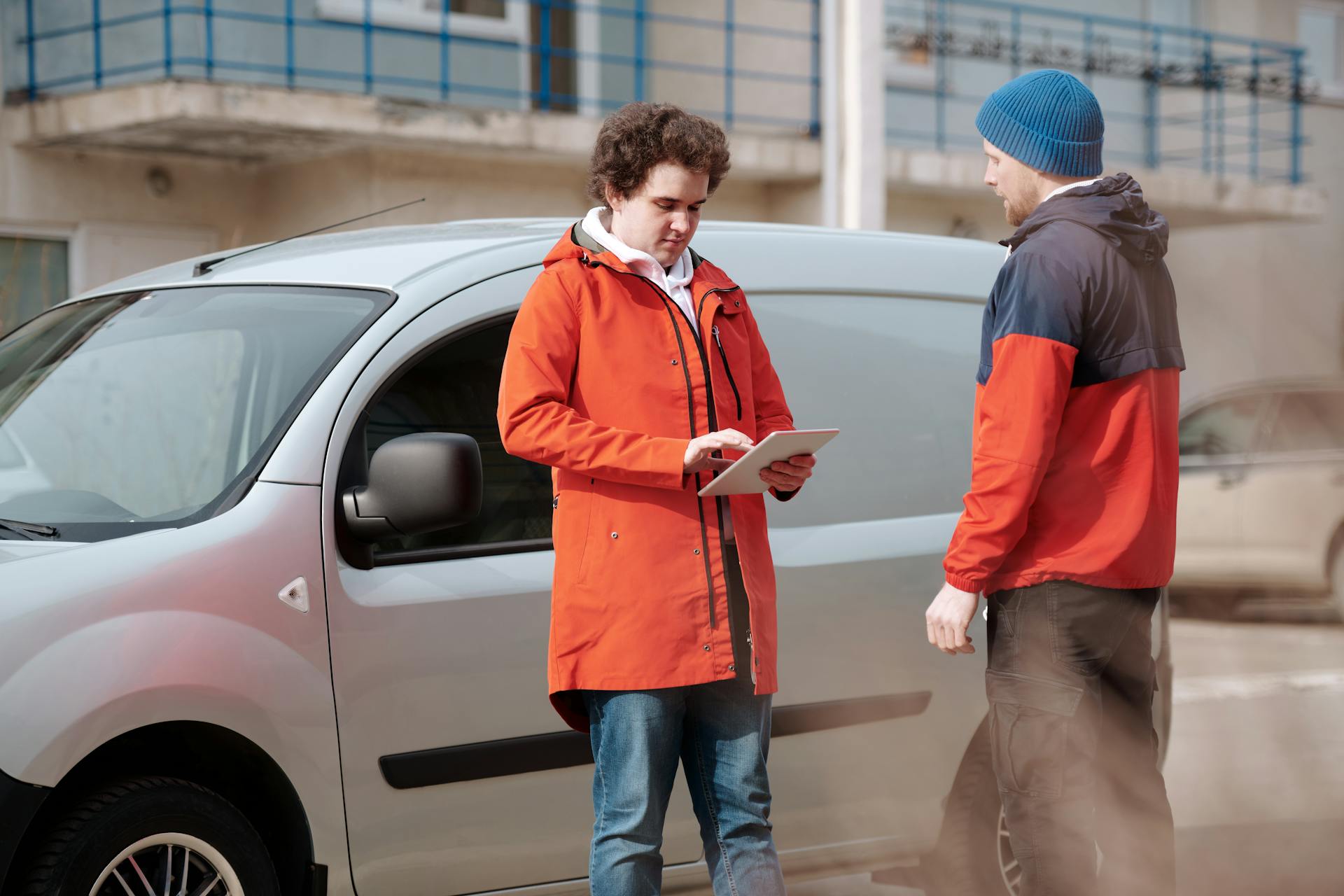 Two delivery men in bright jackets using a digital tablet beside a van outdoors.