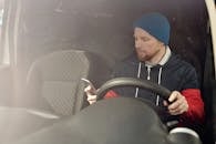 一个留着胡子的男人坐在车里，用智能手机调整日光设置