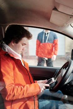 从侧面看，一名送货司机在车内使用数字平板电脑，背景中还有另一个人
