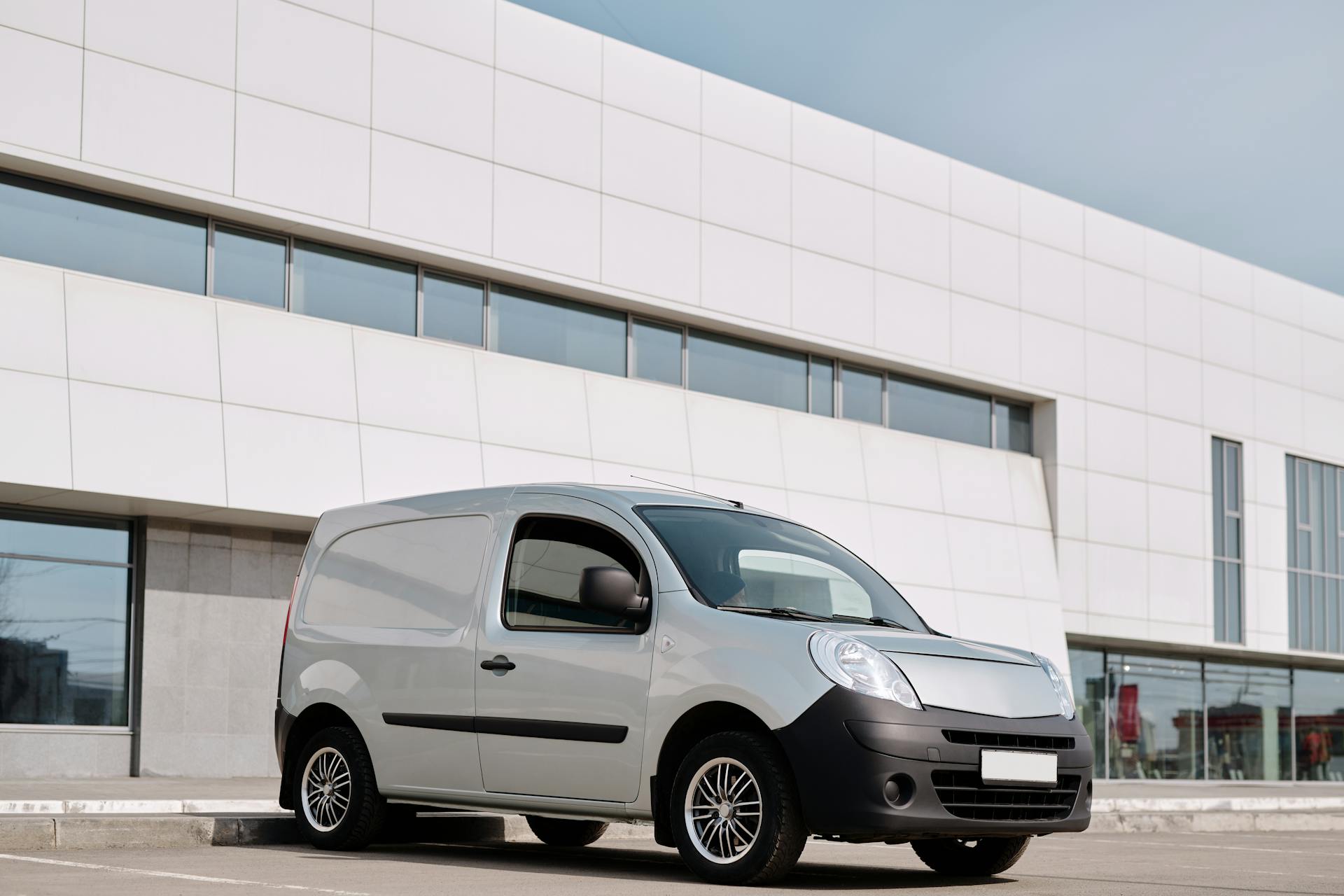 A white delivery van parked in front of a modern office building on a clear day.