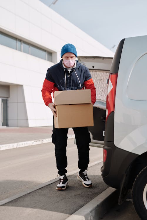 Free Delivery Man Wearing a Face Mask Carrying Boxes Stock Photo