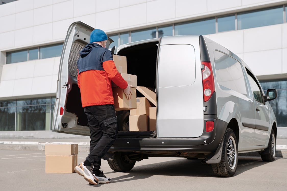 Man in Orange and Blue Long Sleeve Shirt and Black Pants Standing Beside White Van