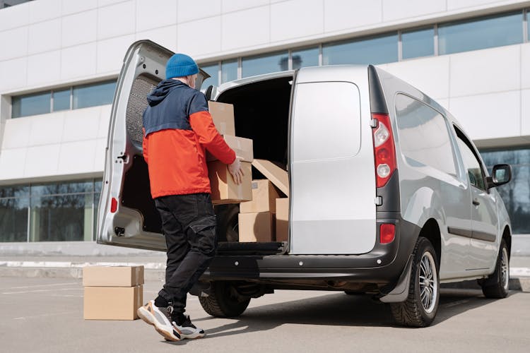 A Man In A Jacket Loading Boxes In A Van