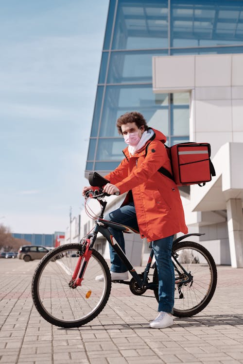Free Delivery Man Wearing a Face Mask and Riding a Bicycle Stock Photo