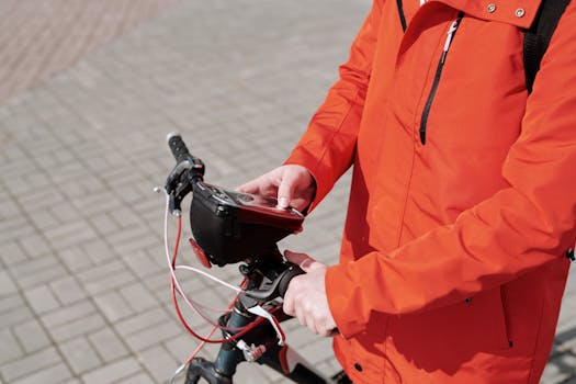 A food delivery cyclist in an orange jacket uses a smartphone while riding in the city.