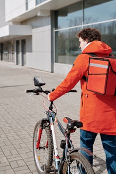 Courier with a bike and thermal bag walking outdoors in urban area.