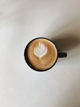 Top-view of a cappuccino featuring beautiful latte art in a black cup on a white surface, perfect for coffee enthusiasts.