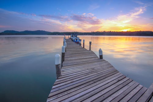 High angle of empty wooden dock leading along peaceful sea against cloudy sunset sky