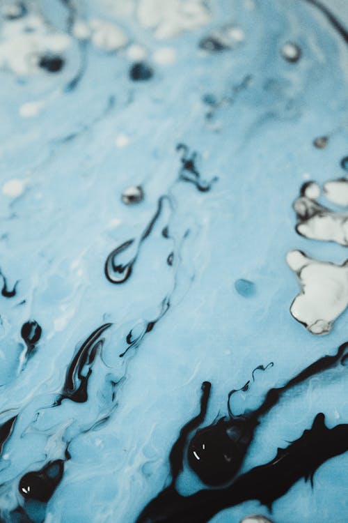 Backdrop of liquid flowing pigment in blue color with black blots smearing and diffusing