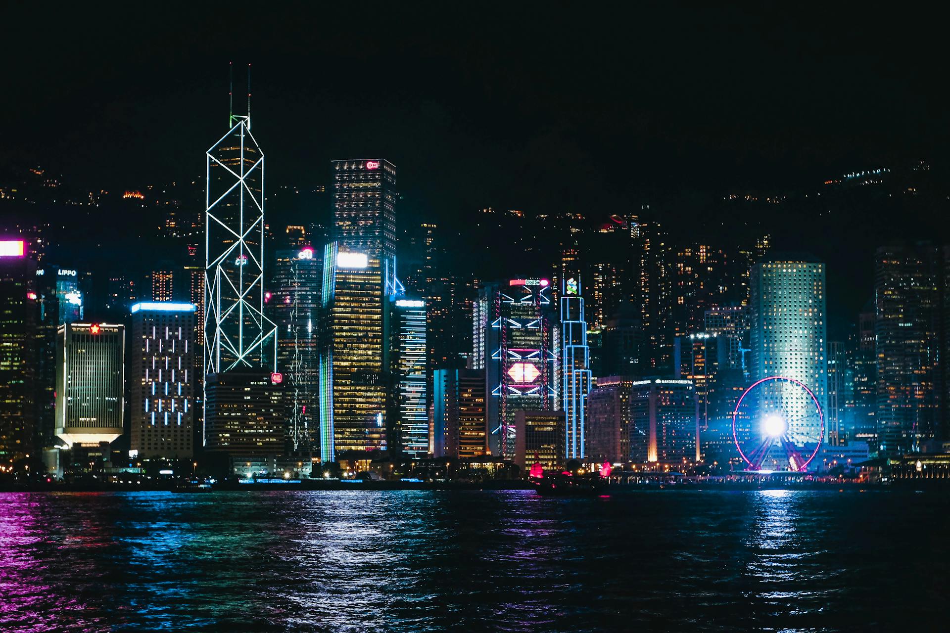 Breathtaking view of Hong Kong skyline at night, featuring illuminated skyscrapers and Ferris wheel by the water.