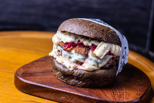 Mouth-watering gourmet burger with dark bun and melted cheese, served on a wooden board.