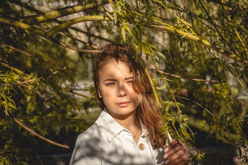 Free Portrait of a young woman in sunlight, surrounded by lush greenery outdoors. Stock Photo