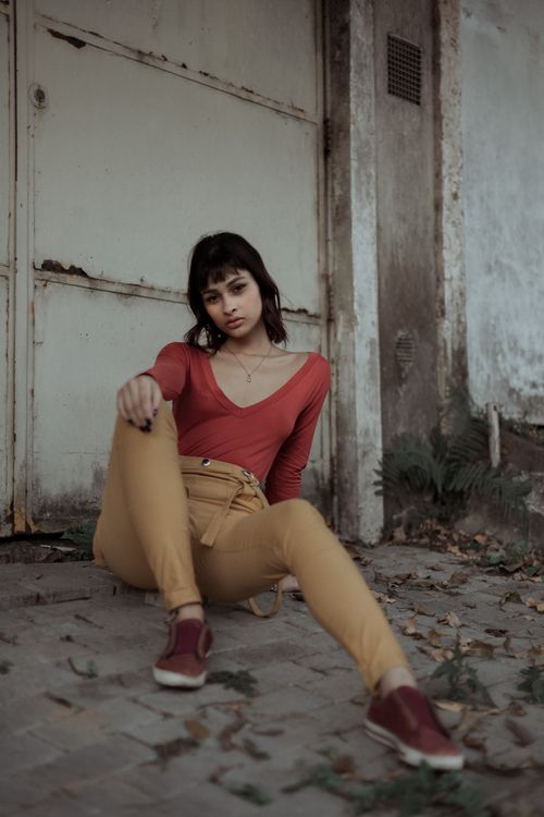 Free Full body of self confident young ethnic female in casual clothes sitting on paved ground near metal shabby door and looking at camera Stock Photo