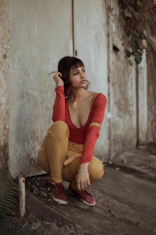 Dreamy young ethnic female sitting on haunches near shabby wall