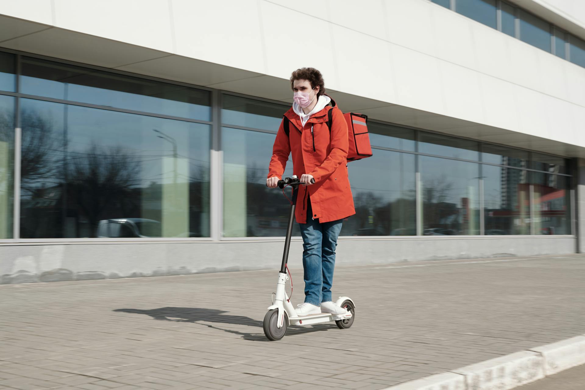A delivery person wears a face mask while riding an electric scooter in the city.