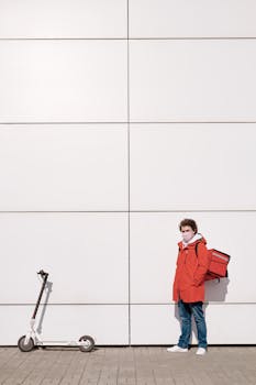 A deliveryman in a face mask stands with a scooter and thermal bag.