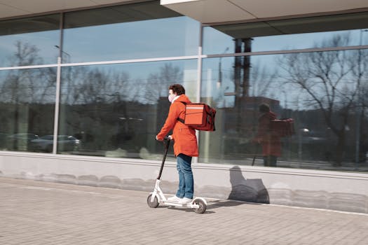 A delivery person wearing a face mask riding an electric scooter with a thermal bag on an urban street.