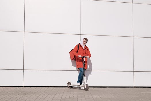Man in red jacket with thermal bag on scooter, urban delivery service.