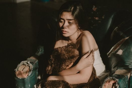 昏暗的房间里，一个女人抱着泰迪熊沉思，流露出深深的情感