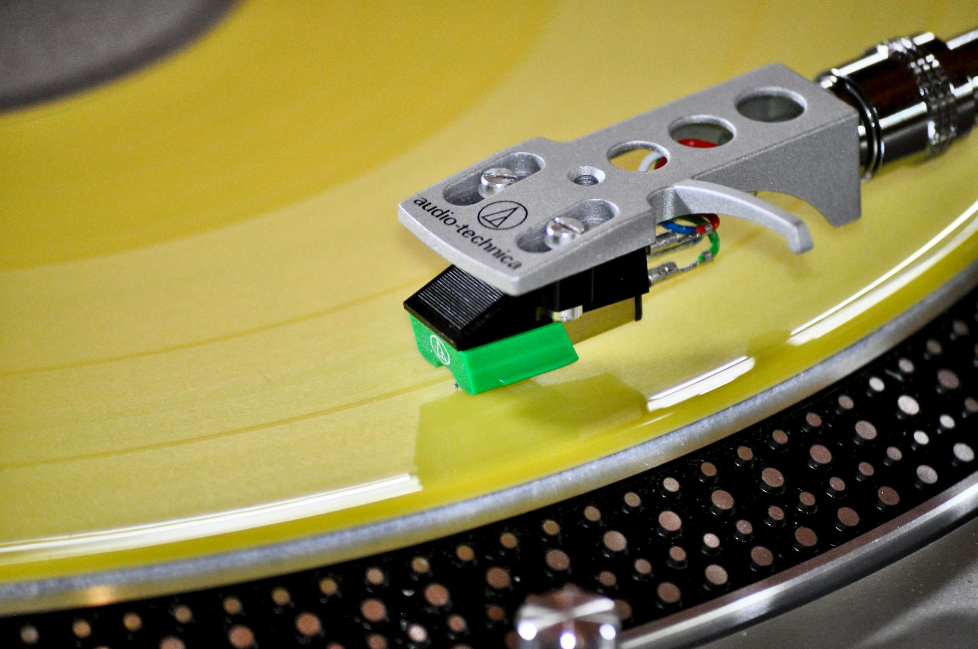 High-quality close-up of a turntable needle on a yellow vinyl record.