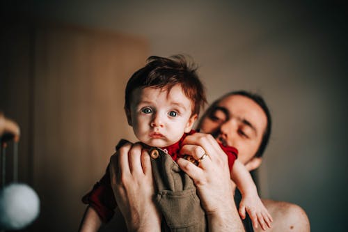Happy young bearded father holding adorable baby boy in hands in light room