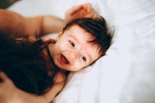 Счастливый младенец играет с родителем в постели