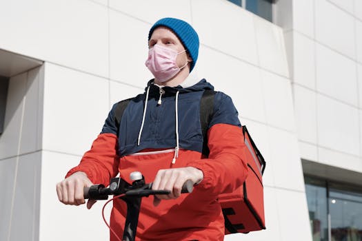 A delivery driver wearing a mask rides a scooter with a thermal bag in a cityscape.