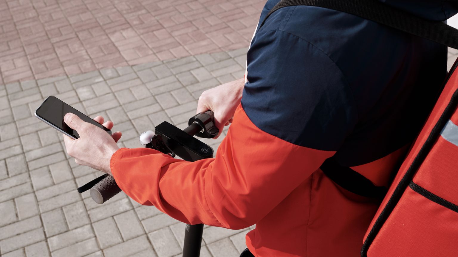 A food delivery courier checking a phone beside an insulated backpack