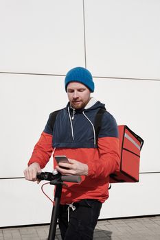 年轻的送货员在户外骑电动滑板车时查看手机