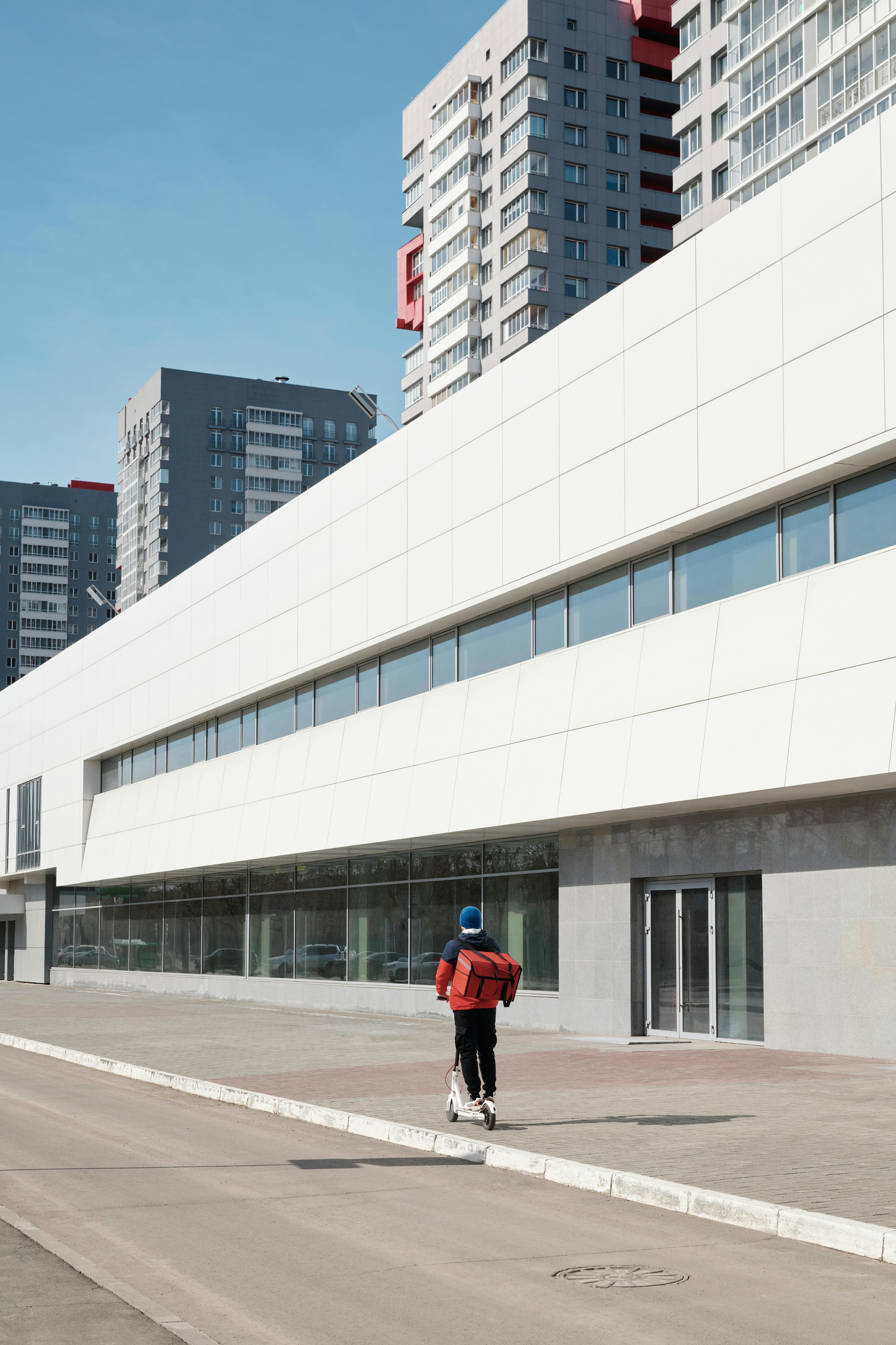 送货员骑着踏板车在城市街道上，穿梭于现代建筑之间运送食物