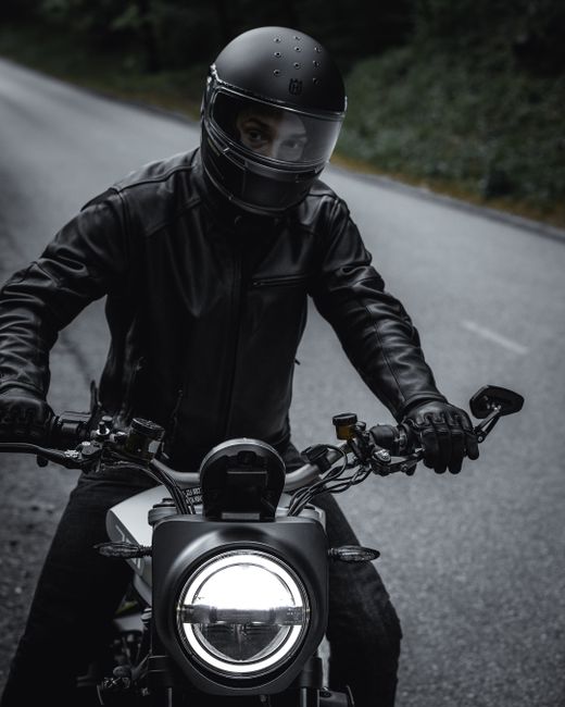 A motorcyclist in a black leather jacket rides along a forest road in Slovenia.
