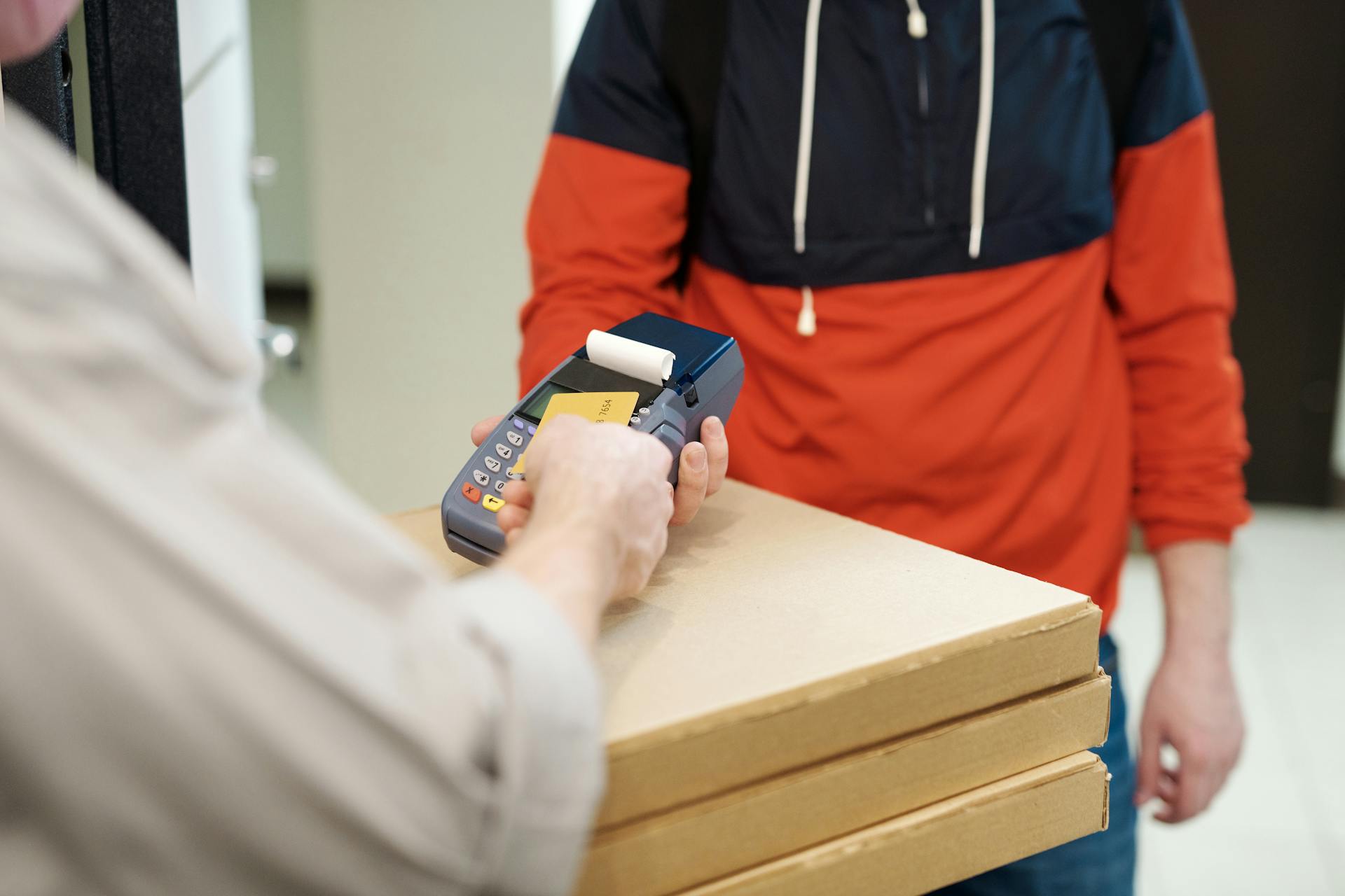 Customer making a contactless payment to a delivery person with a card reader and pizza boxes.